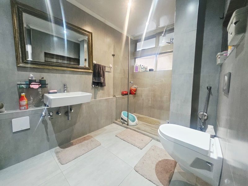 Modern bathroom featuring a wall-mounted basin, wall-hung toilet, and a spacious walk-in shower with a glass screen and neutral floor-to-ceiling tiling.