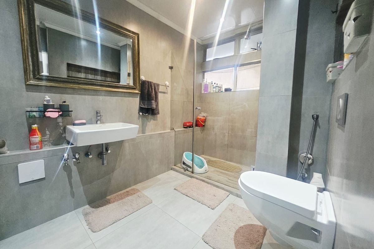 Modern bathroom featuring a wall-mounted basin, wall-hung toilet, and a spacious walk-in shower with a glass screen and neutral floor-to-ceiling tiling.