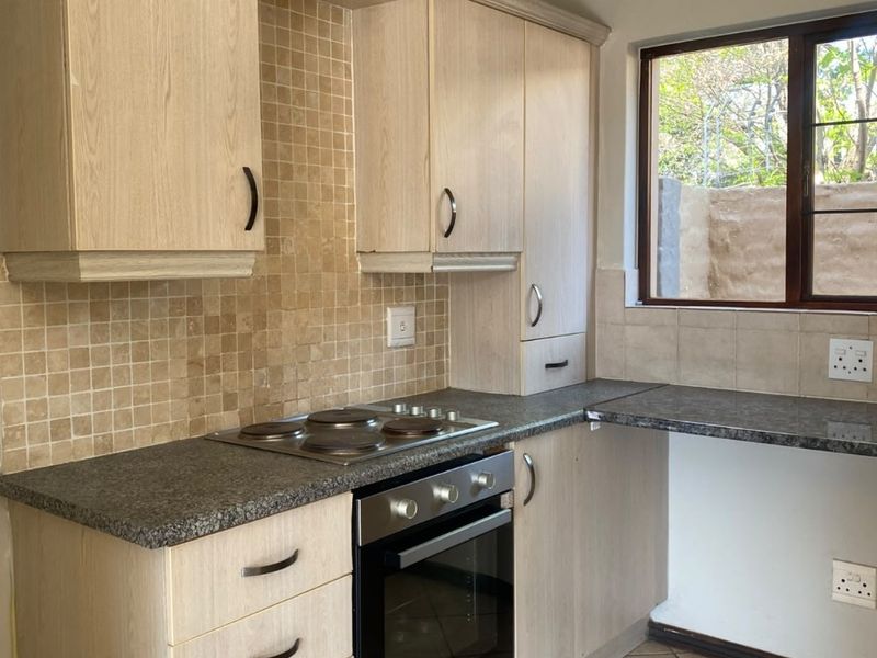 A functional kitchen featuring light wood-look cabinetry, granite countertops, a mosaic tile backsplash, and integrated oven and hob, with ceramic floor tiling.