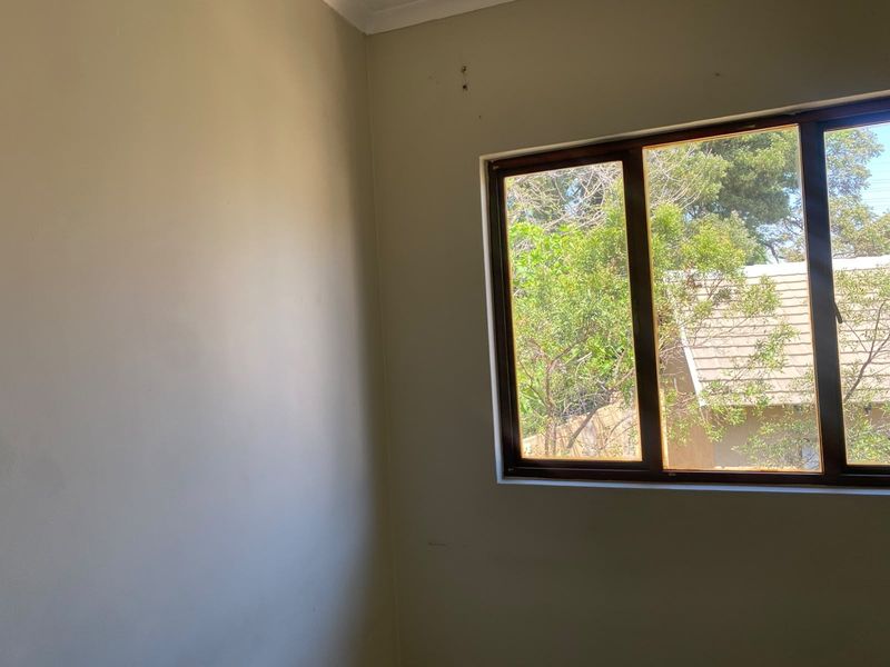 A vacant bedroom featuring a timber-framed window with a view of the garden and mature trees.