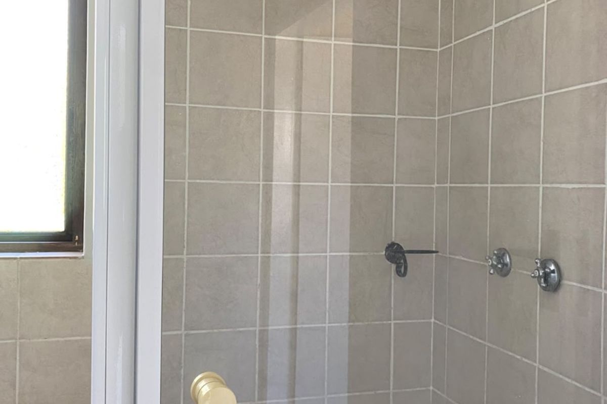 A functional bathroom shower area featuring neutral wall tiles, a glass door, and standard chrome shower fixtures.