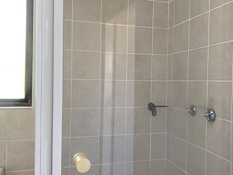 A functional bathroom shower area featuring neutral wall tiles, a glass door, and standard chrome shower fixtures.