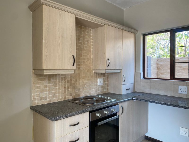 A functional kitchen featuring light wood-finish cabinetry, granite countertops, a mosaic tile backsplash, and integrated electric cooking appliances.