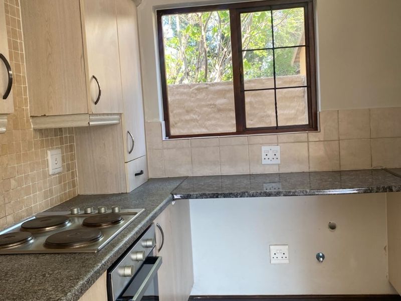 A functional kitchen featuring built-in cabinetry, granite countertops, an electric hob, and an oven, with tiled flooring and backsplash throughout.