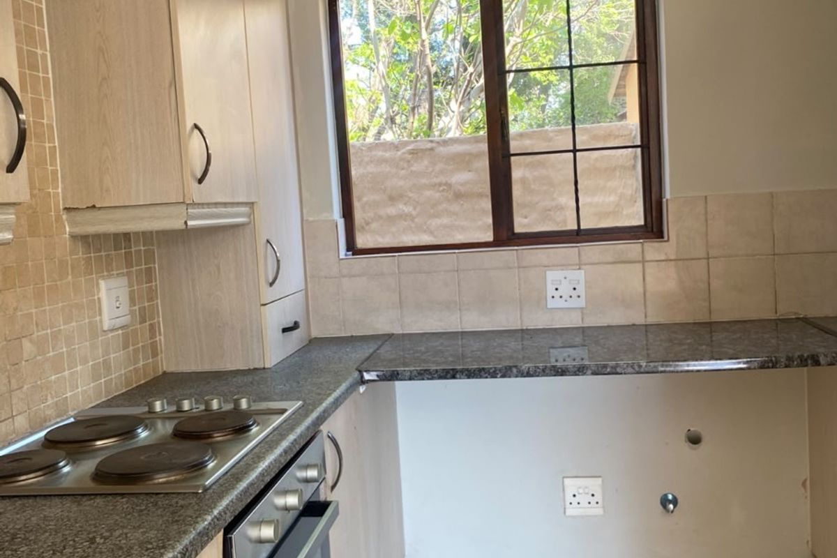 A functional kitchen featuring built-in cabinetry, granite countertops, an electric hob, and an oven, with tiled flooring and backsplash throughout.