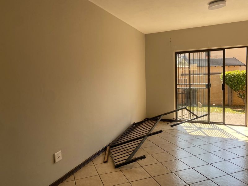 An empty bedroom featuring tiled flooring, neutral walls, and a sliding glass door with a security gate leading to the exterior.