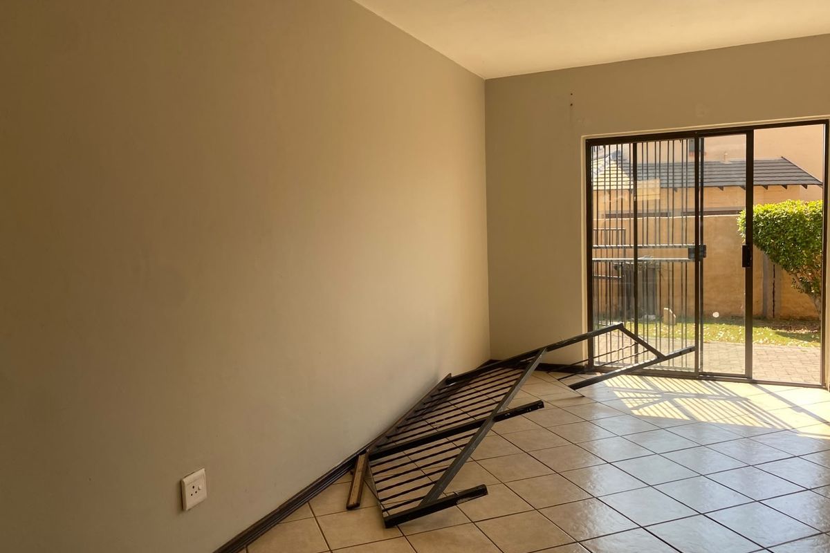 An empty bedroom featuring tiled flooring, neutral walls, and a sliding glass door with a security gate leading to the exterior.