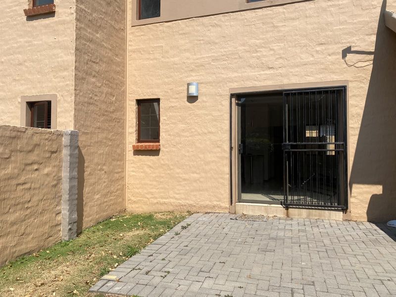 Rear exterior view featuring a paved patio area, sliding door access with a security gate, and a brick boundary wall.