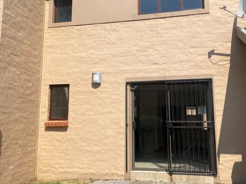 Rear exterior view of the property featuring a paved patio area, sliding glass door with security gate, and exterior wall lighting.