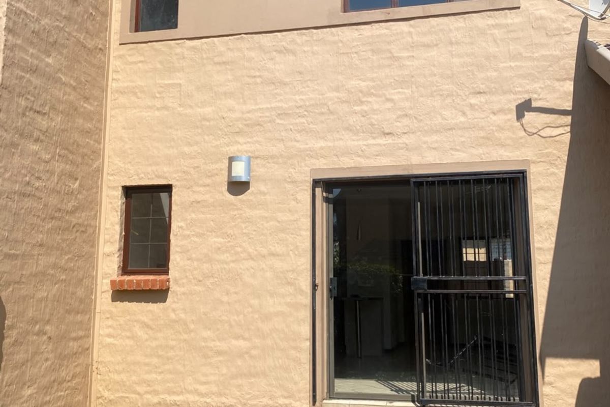 Rear exterior view of the property featuring a paved patio area, sliding glass door with security gate, and exterior wall lighting.