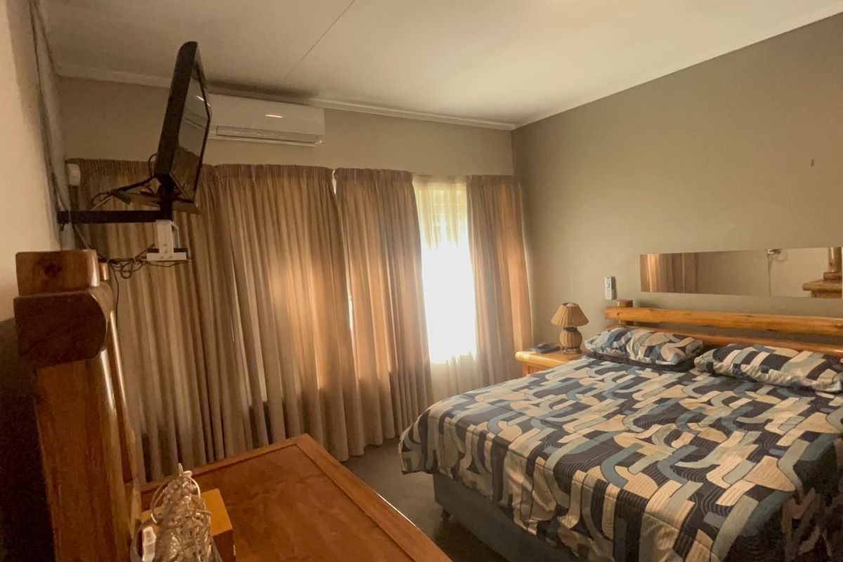 A functional bedroom featuring a wall-mounted air conditioning unit, neutral wall finishes, and large window curtains.