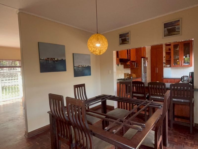 Open-plan dining area featuring warm parquet flooring, flowing into a functional kitchen with built-in cabinetry and a breakfast bar counter.