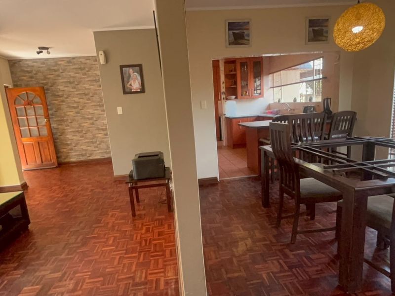 Open plan living and dining area featuring parquet flooring, a stone veneer feature wall, and a view into the adjacent kitchen space.