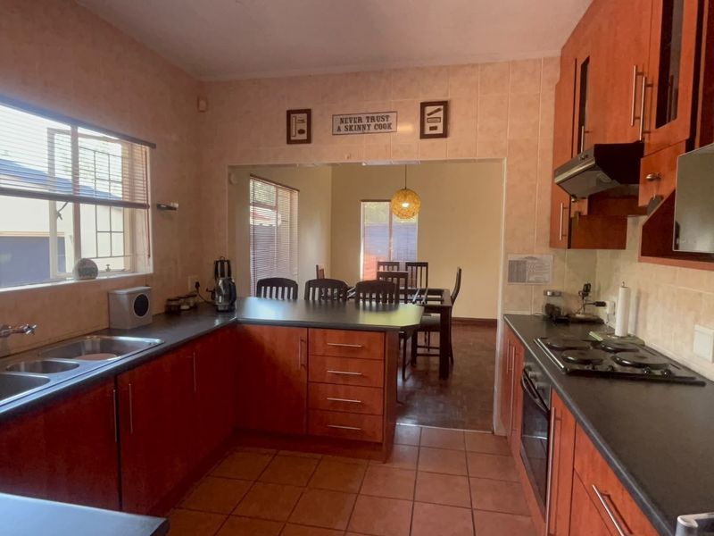 A functional kitchen featuring wooden cabinetry, dark countertops, built-in oven and hob, and tiled finishes, with an open-plan flow into the dining area.