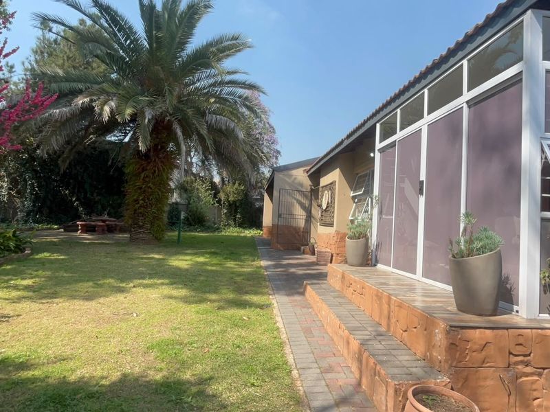 A well-maintained rear garden featuring a paved patio area, brick steps, and an enclosed sunroom extension.