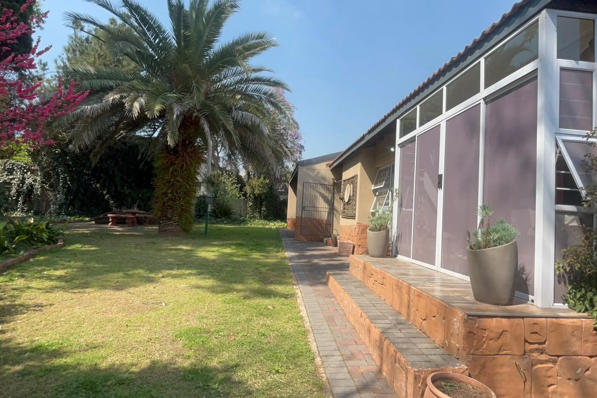 A well-maintained rear garden featuring a paved patio area, brick steps, and an enclosed sunroom extension.