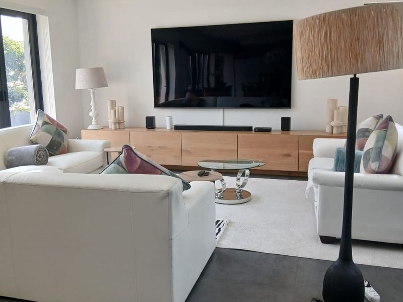 A modern, well-maintained living room featuring large-format floor tiles, recessed ceiling lighting, and custom built-in cabinetry for media storage.