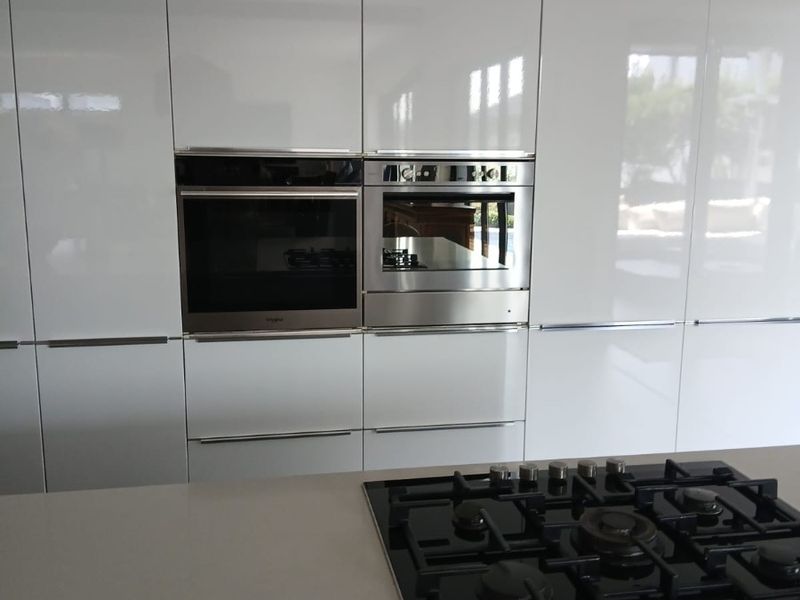 Modern kitchen featuring high-gloss cabinetry, integrated stainless steel oven and microwave, and a sleek gas cooktop set into a stone countertop.