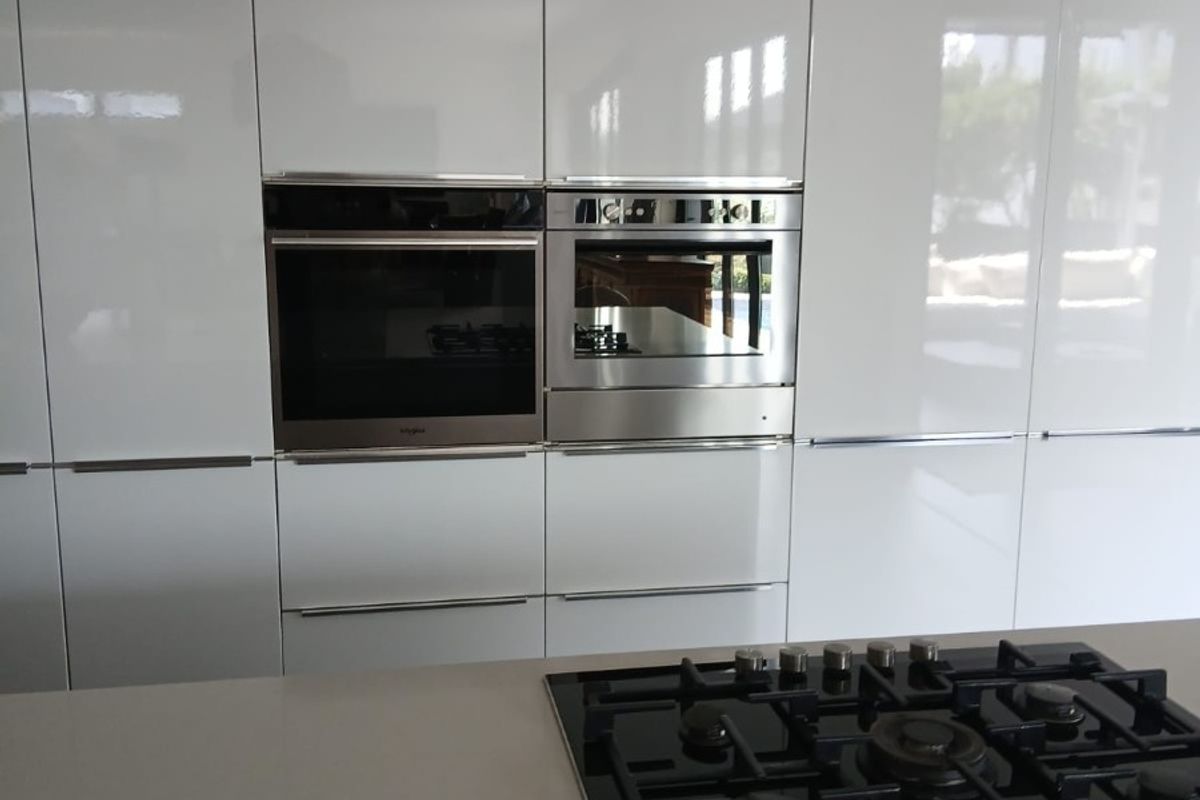 Modern kitchen featuring high-gloss cabinetry, integrated stainless steel oven and microwave, and a sleek gas cooktop set into a stone countertop.