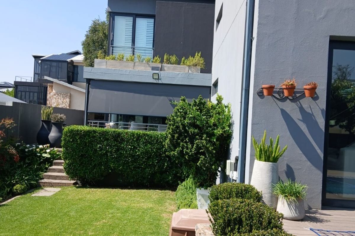 A well-maintained rear garden featuring a timber deck, stone retaining wall, and manicured hedges, adjacent to a modern multi-story residential building.