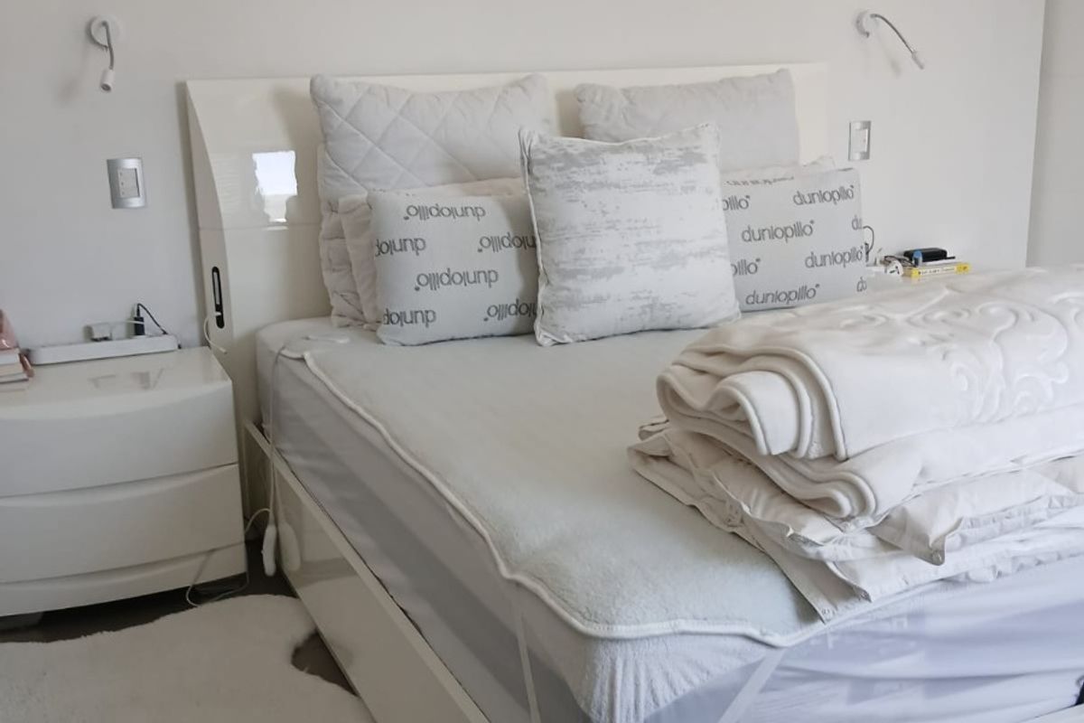 A bright and neutral bedroom featuring wall-mounted reading lights and integrated electrical fixtures.