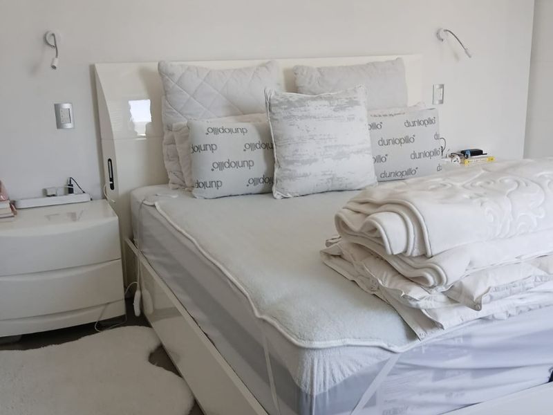 A bright and neutral bedroom featuring wall-mounted reading lights and integrated electrical fixtures.