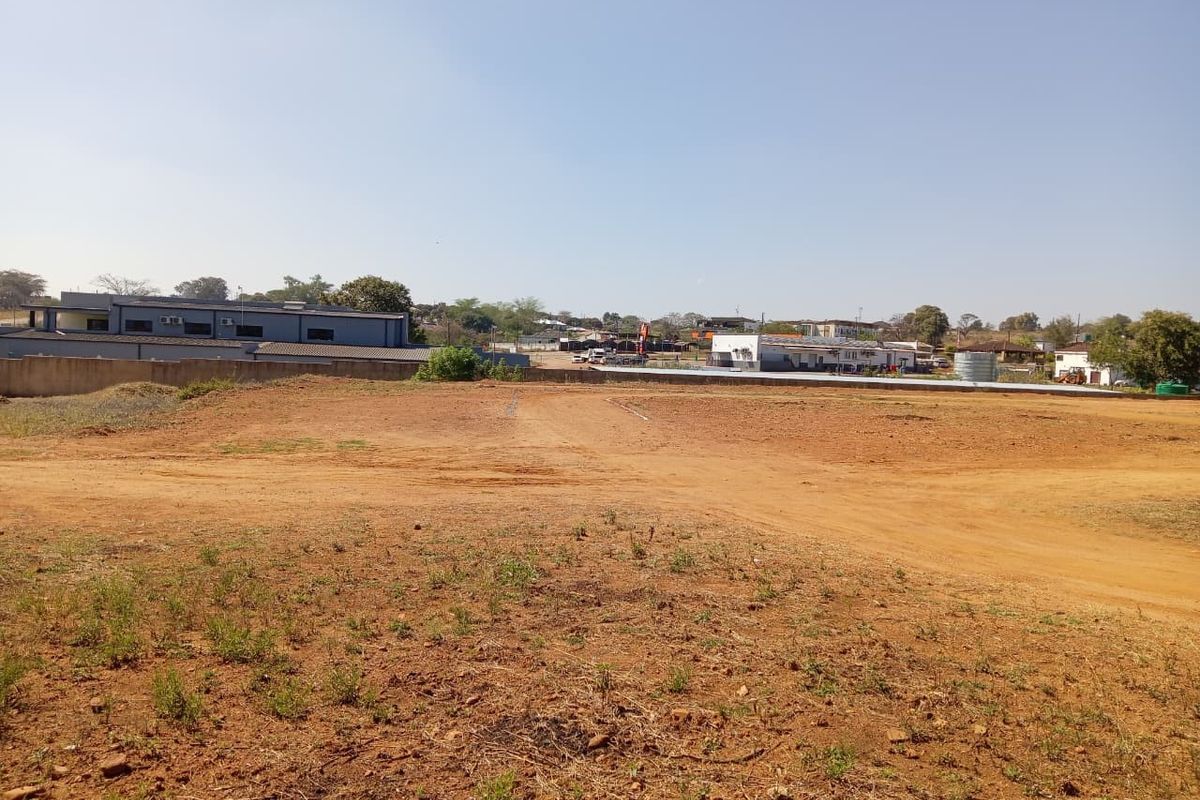 A wide-angle view of a vacant commercial land plot featuring cleared ground and a perimeter wall, suitable for future development.