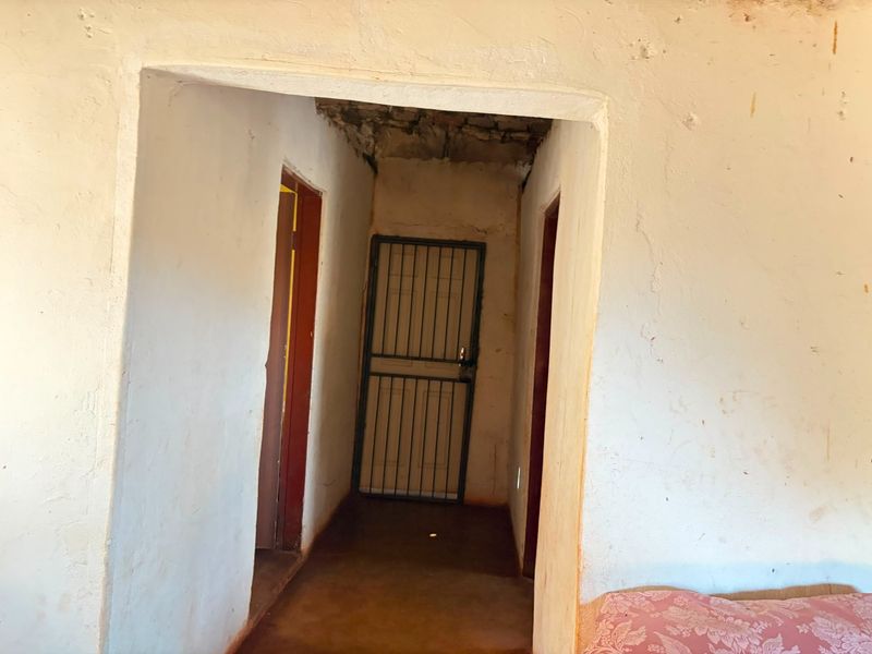 A narrow hallway featuring a security gate, internal doors, and concrete flooring, showing significant signs of wear and requiring structural repairs and cosmetic updates.
