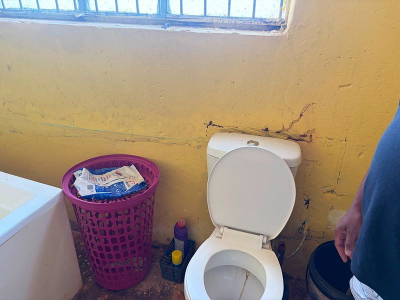 A bathroom featuring a standard toilet and bathtub, currently showing significant wear and tear on the wall finishes requiring maintenance and repair.
