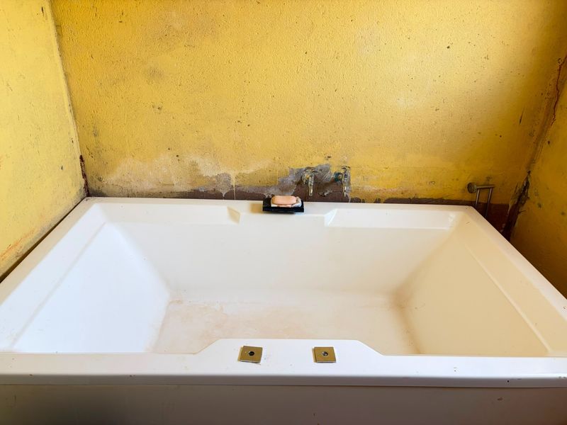 A bathroom featuring a built-in bathtub with exposed plumbing fixtures, requiring significant wall repairs and cosmetic updates to improve the overall condition.