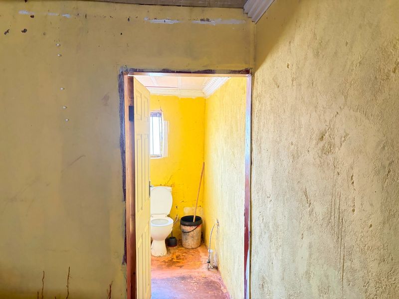 A small, dated bathroom requiring significant renovation, featuring basic toilet fixtures and worn wall and floor finishes.
