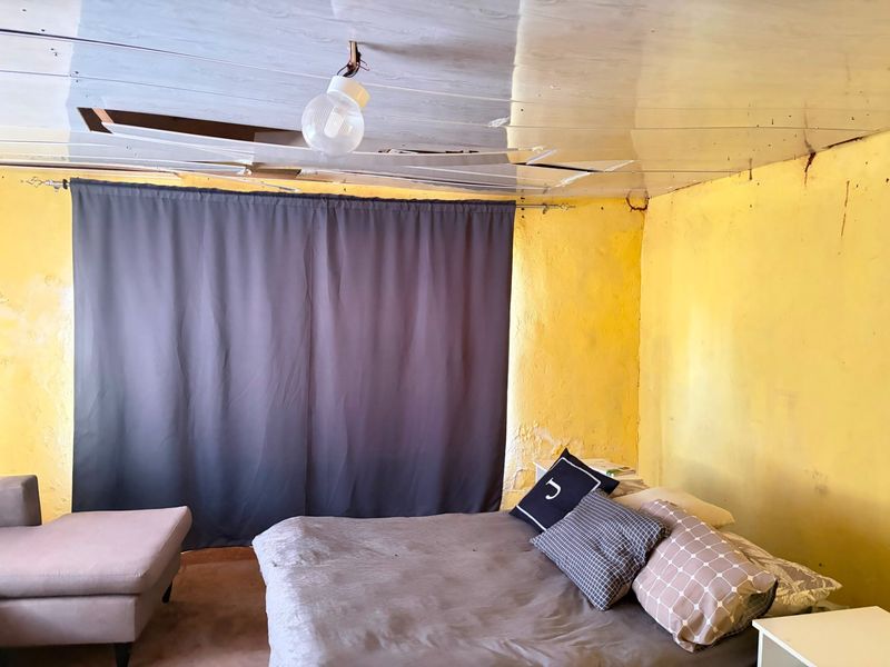 A bedroom space requiring significant renovation, featuring damaged ceiling panels, exposed electrical wiring, and deteriorating wall finishes.