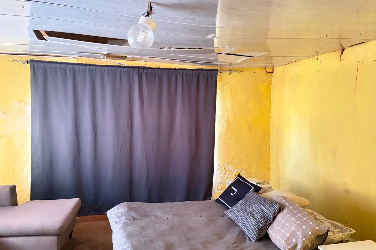 A bedroom space requiring significant renovation, featuring damaged ceiling panels, exposed electrical wiring, and deteriorating wall finishes.
