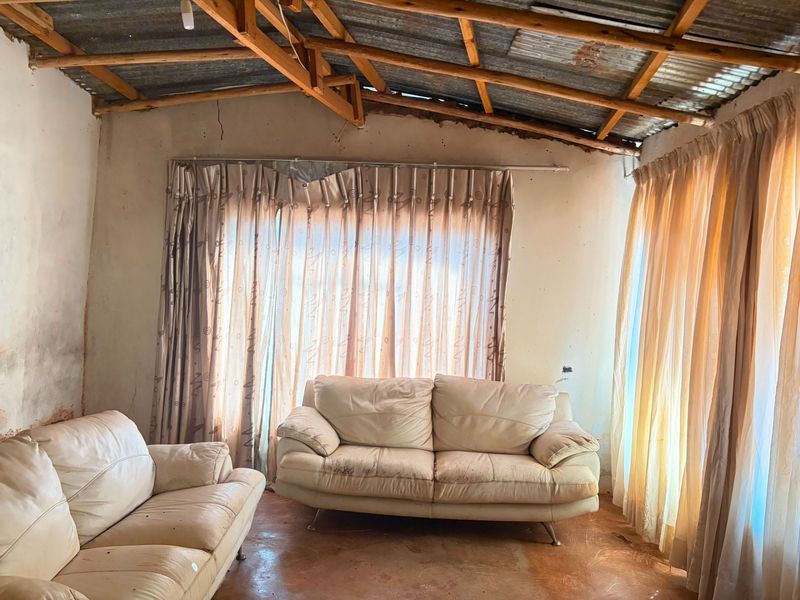 Living room featuring exposed timber roof trusses, corrugated metal ceiling, and concrete flooring, requiring significant renovation and cosmetic updates.