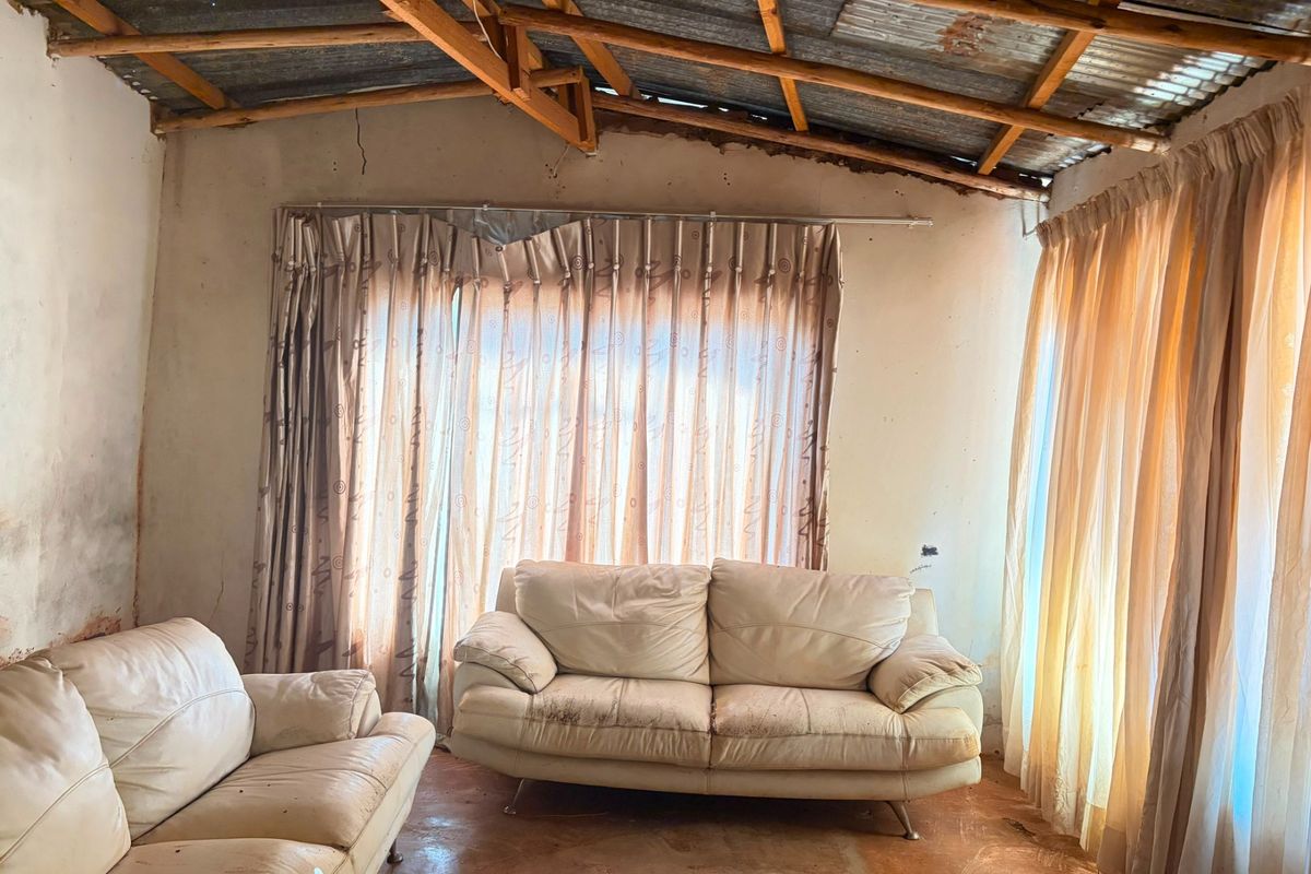 Living room featuring exposed timber roof trusses, corrugated metal ceiling, and concrete flooring, requiring significant renovation and cosmetic updates.