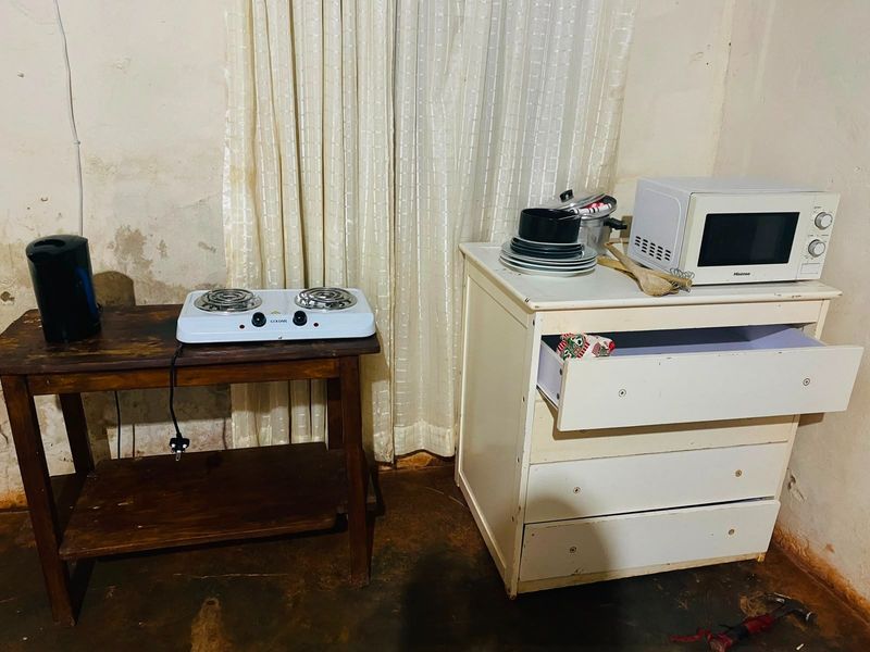 A basic kitchen setup featuring a portable electric hob and microwave, showing significant wear to the walls and flooring.