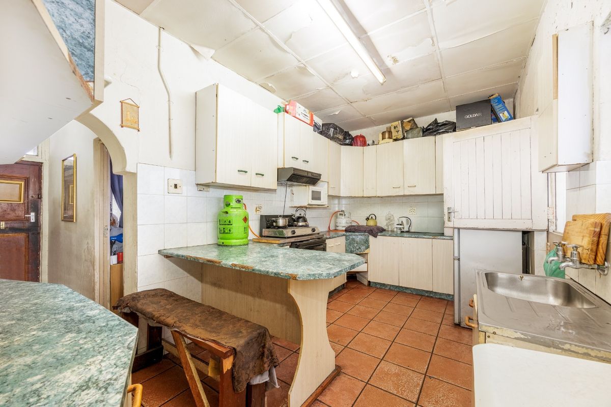 A dated kitchen featuring built-in cabinetry, laminate countertops, and tiled flooring, requiring significant cosmetic updates and ceiling repairs.