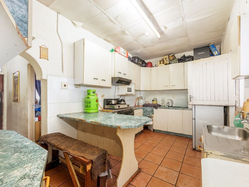 A dated kitchen featuring built-in cabinetry, laminate countertops, and tiled flooring, requiring significant cosmetic updates and ceiling repairs.