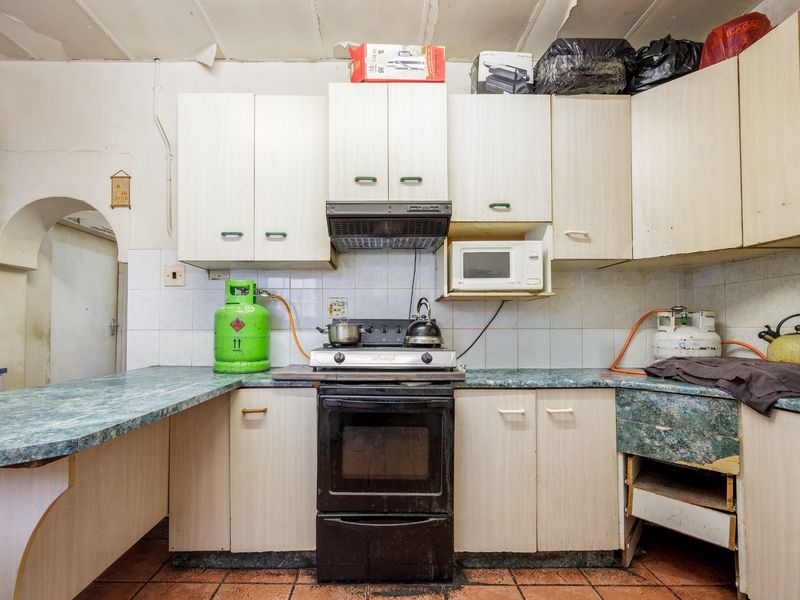 A dated kitchen featuring laminate cabinetry, a gas stove, and tiled finishes, currently requiring significant maintenance and cosmetic updates to improve functionality and aesthetic appeal.