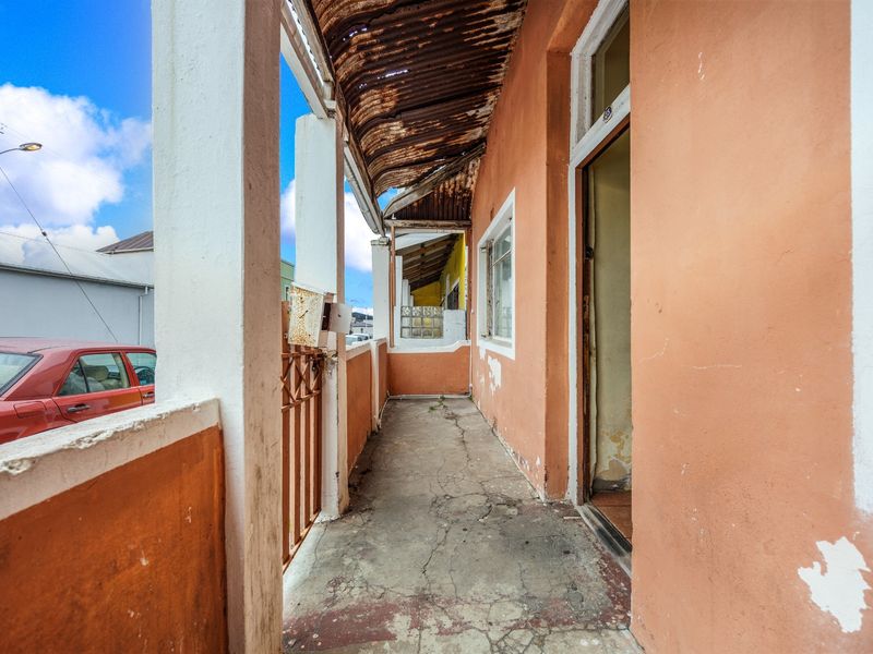 A weathered covered patio area featuring concrete flooring, structural pillars, and a corrugated iron roof in need of maintenance and refurbishment.