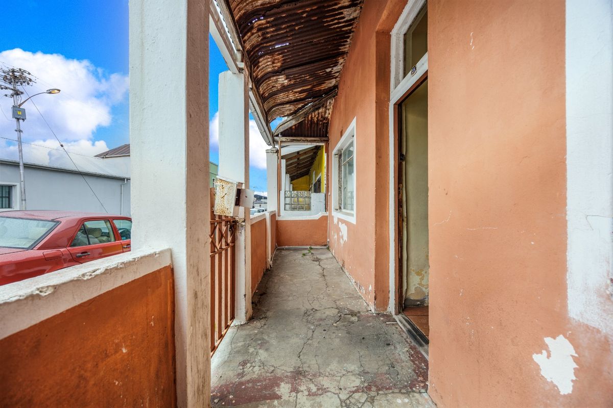 A weathered covered patio area featuring concrete flooring, structural pillars, and a corrugated iron roof in need of maintenance and refurbishment.