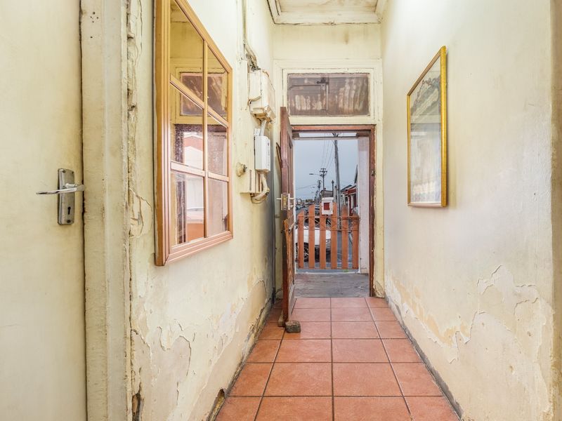 A narrow hallway featuring tiled flooring and a wooden door leading to the exterior, showing significant wear to the wall finishes.