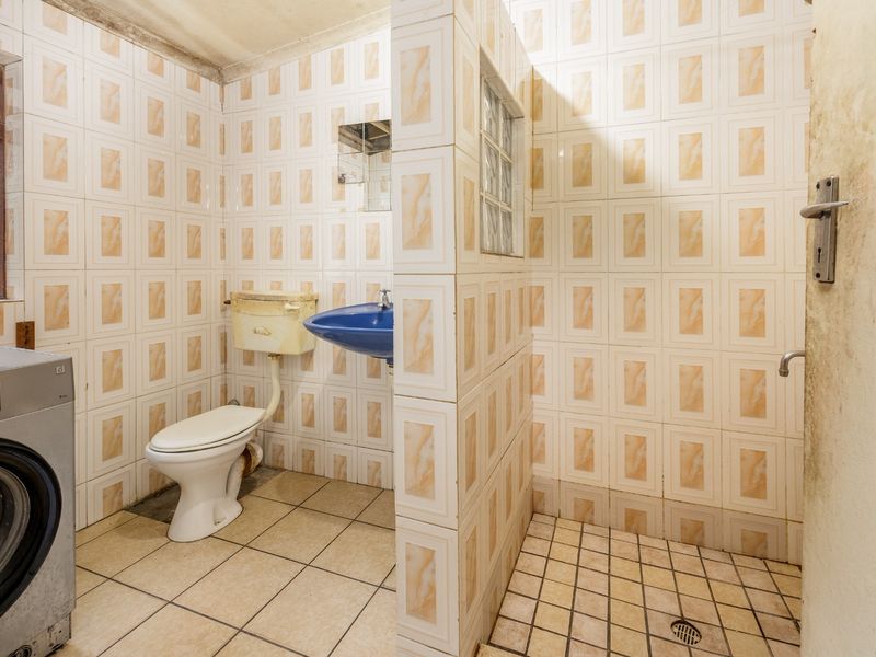 A dated bathroom featuring a wall-mounted basin, toilet, and walk-in shower area with tiled finishes, requiring renovation to modernize the space.