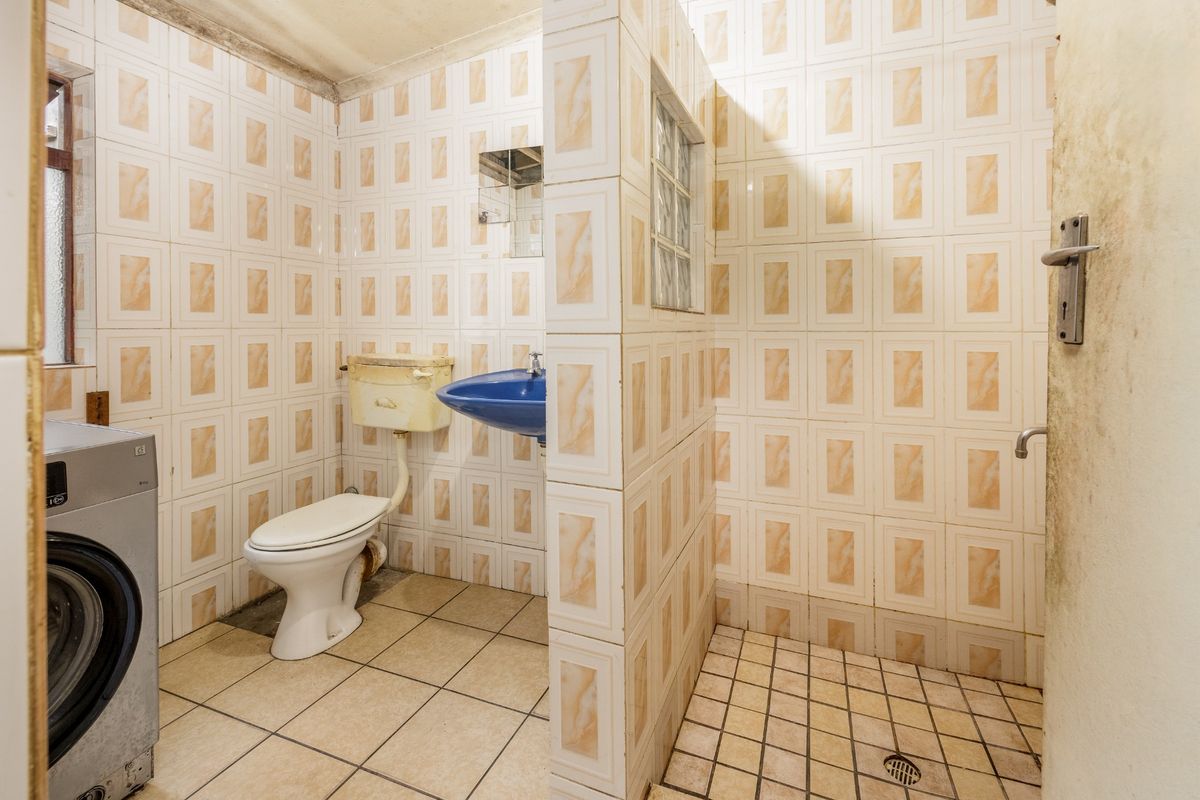 A dated bathroom featuring a wall-mounted basin, toilet, and walk-in shower area with tiled finishes, requiring renovation to modernize the space.