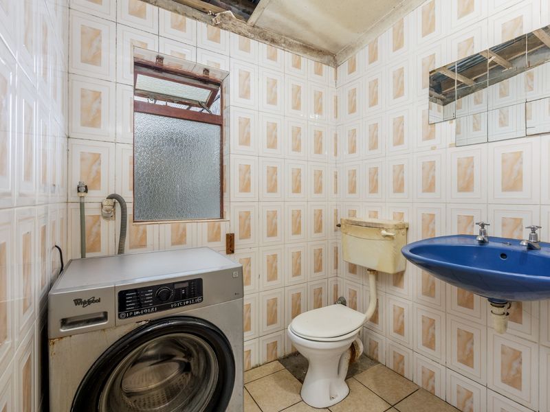 A dated bathroom featuring a blue wall-mounted basin, toilet, and tiled finishes, requiring significant renovation and repair to the ceiling and fixtures.