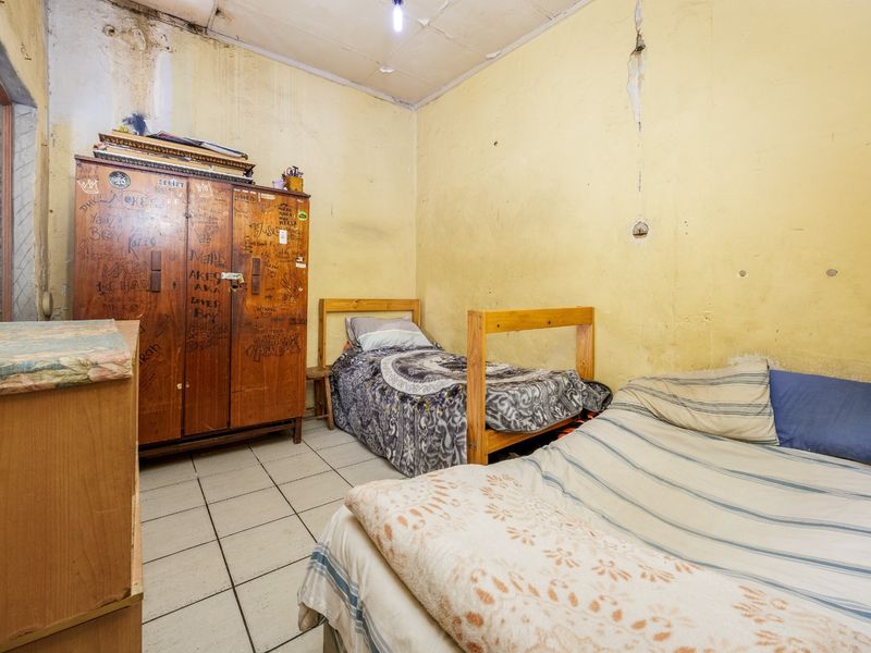 A bedroom featuring tiled flooring and ceiling tiles, currently showing significant signs of wear including wall damage and staining requiring renovation.