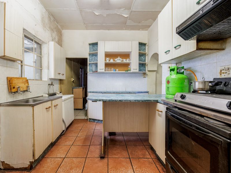 A dated kitchen featuring laminate cabinetry, tiled flooring, and a breakfast bar, requiring significant renovation and cosmetic updates to modernize the space.