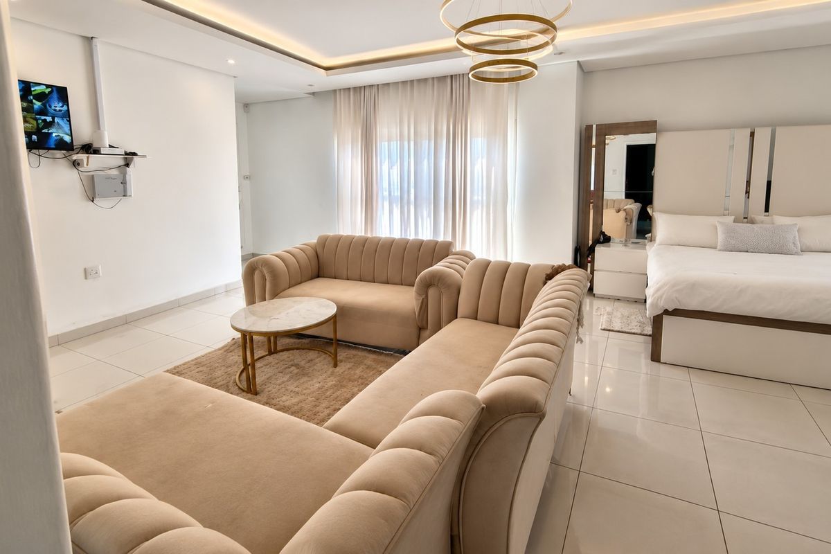 A modern open-plan living and sleeping area featuring neutral tones, tiled flooring, and recessed ceiling lighting.