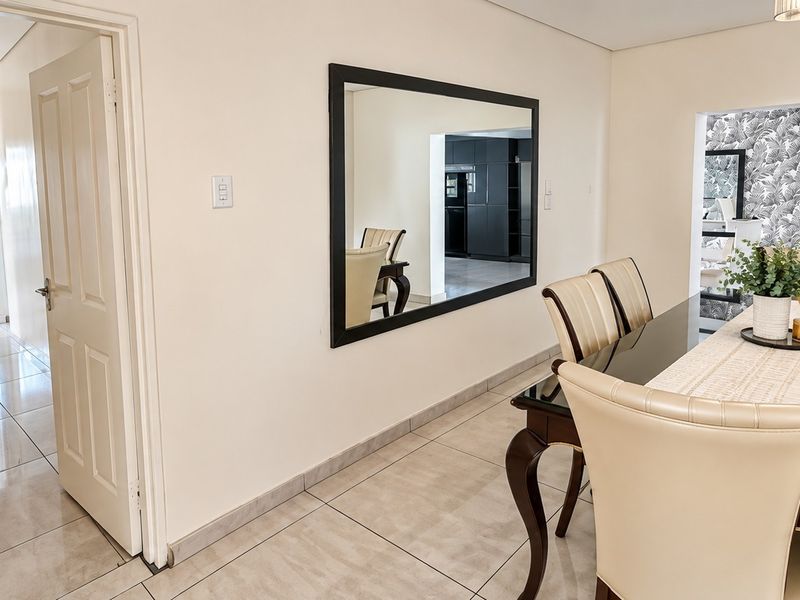 A bright dining room featuring neutral tiled flooring, recessed ceiling lighting, and a view through to the kitchen area.