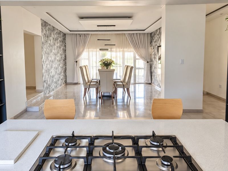 Modern open-plan living area featuring a sleek kitchen island with gas hob, flowing into a bright dining space with elegant finishes.